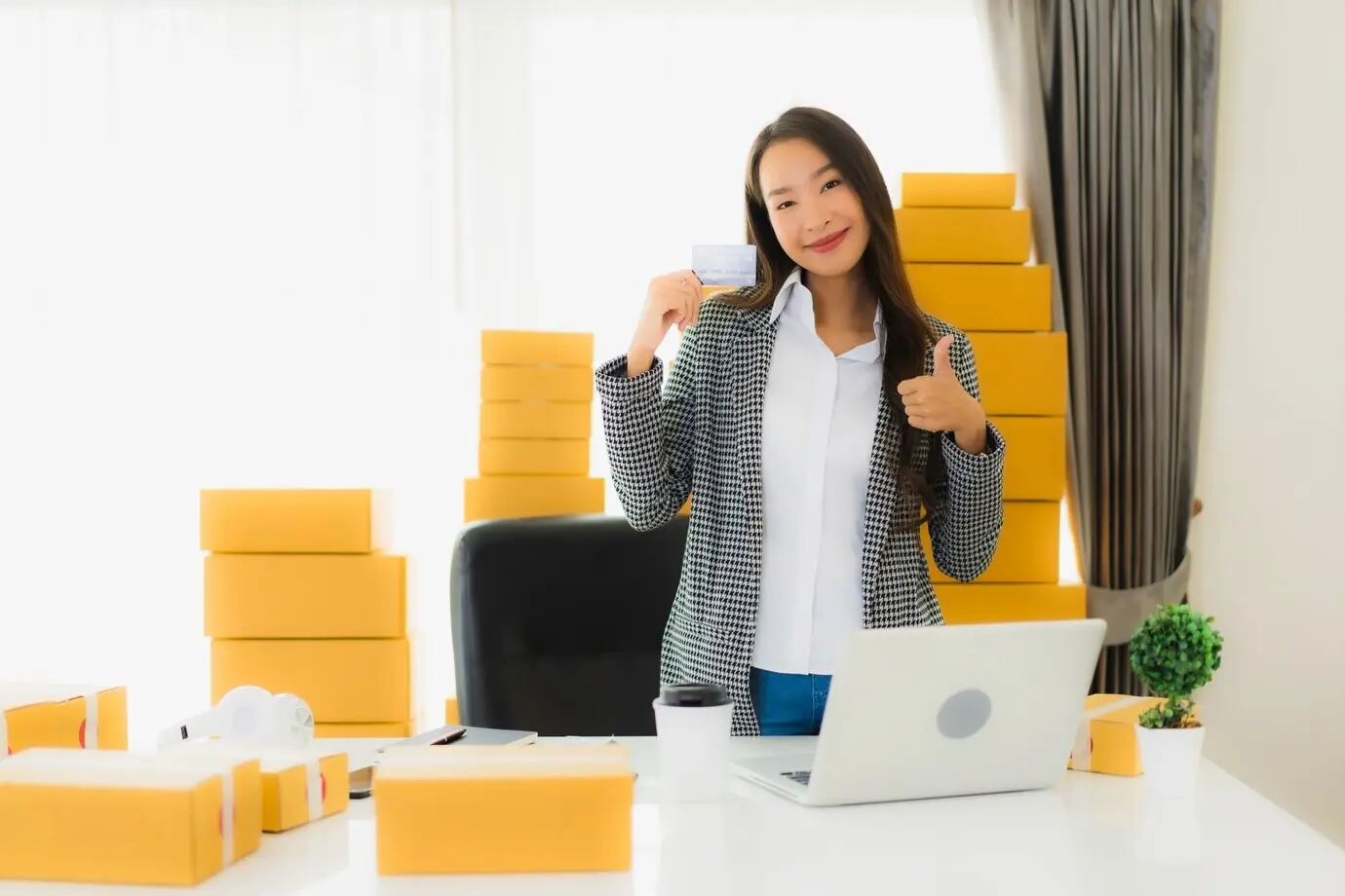 Porträt einer schönen jungen asiatischen Frau, die von zu Hause aus arbeitet, mit Kreditkarte und einem Pappkarton, der für den Versand von Einkäufen bereitsteht.